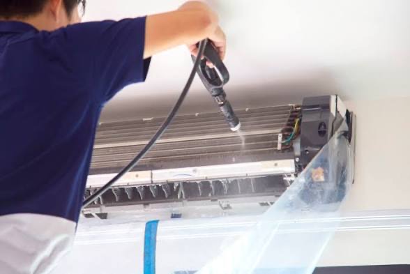 A technician flushing the evaporator coil of an opened mini-split with a low-pressure spray wand